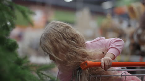 A-little-girl-in-a-grocery-cart-looks-at-a-Christmas-tree-in-slow-motion.